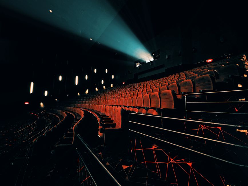 Cultura Pop — Dark, empty theater with dramatic seat lighting and projector beam.