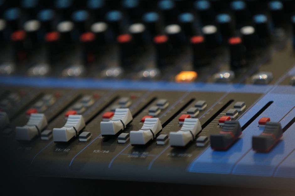 Cultura Pop — Close-up of an advanced audio mixing panel with slide controls and knobs in a studio setting.